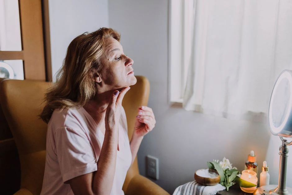 Mature woman examining her skin in a well-lit room during the later recovery period